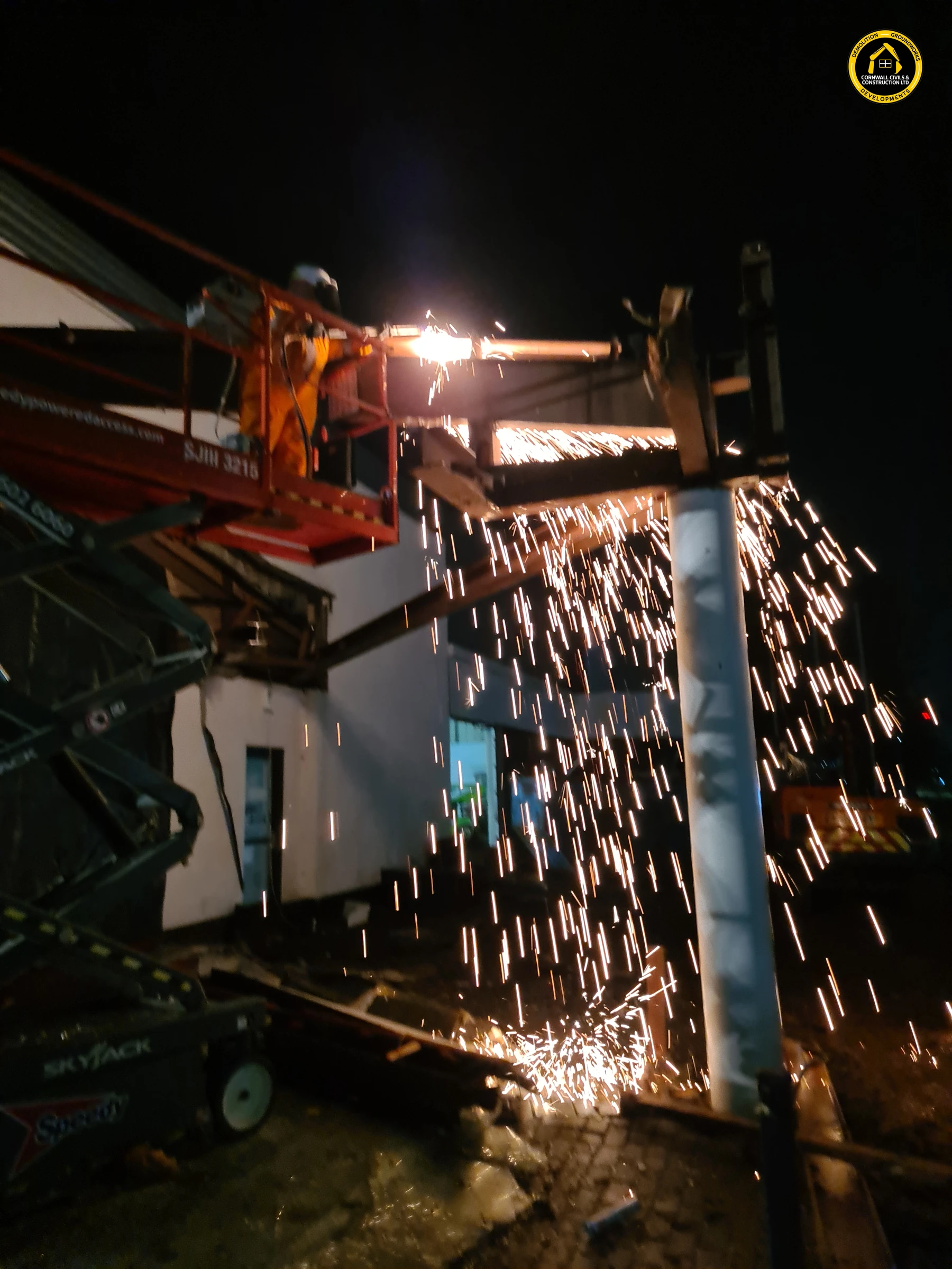 Night demolition of the BMW dealership with hot cutting sparks down the glazed facade in Exeter